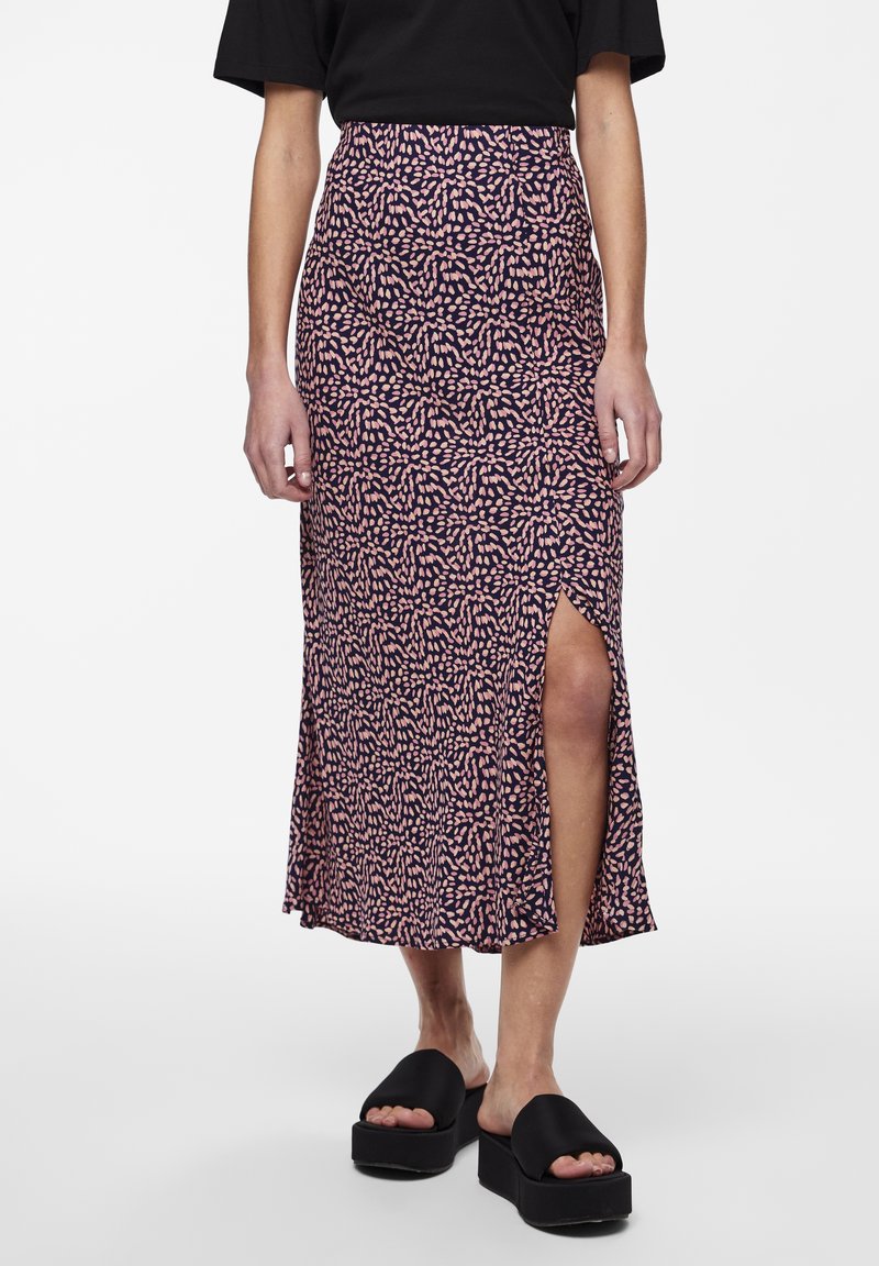 Femme portant un haut noir et une jupe midi à motif avec une fente latérale, associée à des sandales à plateforme noires.