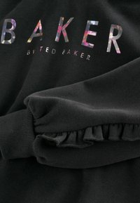 Čierna mikina s logom "BAKER" v farebných reflexných písmenách. Obsahuje volánový lem a mäkkú textúru látky.
