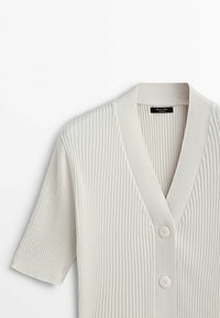 Cardigan beige en tricot côtelé à manches courtes avec un col en V profond et deux boutons ronds à l'avant.