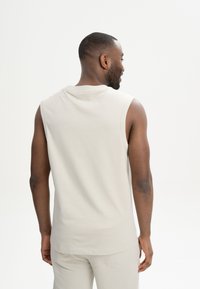 Helles beige ärmelloses Shirt mit rundem Ausschnitt und weicher Textur, das eine lockere Passform und ein einfaches Design betont.