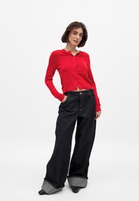 Pikad punased pikkade varrukatega kardigan ümara krae ja nööpidega, millele on sobitatud laiad mustad denim-püksid, millel on üles keeratud säär ja kontrastne sisekate.