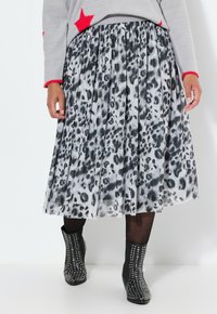 Gonna plissettata in tessuto leggero con motivo leopardato monocromatico. Abbinata a stivali alla caviglia decorati con borchie argentate.