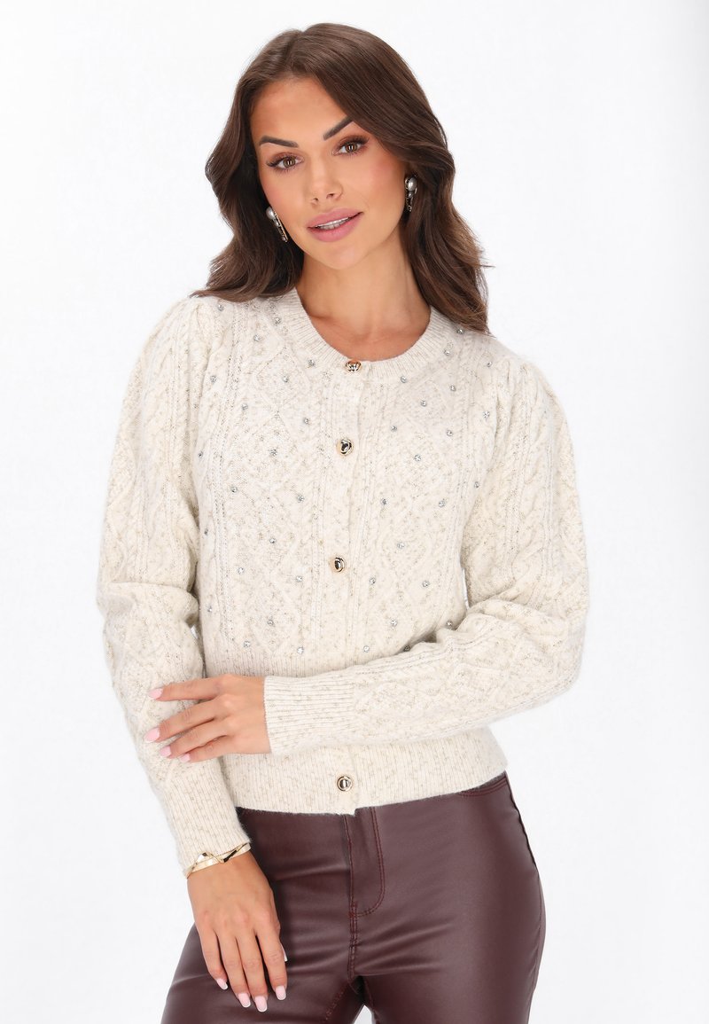 Könnyű bézs kötött kardigán texturált mintával, kerek nyakkivágással és dekoratív gombokkal. Elöl gyöngyös díszítésekkel rendelkezik.