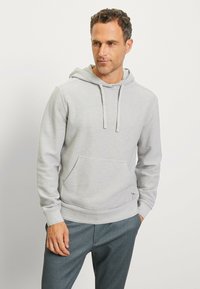 Gray hoodie with a front pocket, drawstring hood, and ribbed cuffs. Paired with dark gray pants. Soft fabric and simple design.