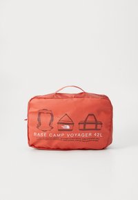 Compact red travel bag labeled "Base Camp Voyager 42L" with illustrations of backpack, duffel, and carry handles on front.