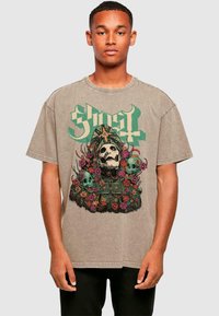 Graphic oversized t-shirt in tan, featuring a central illustration of a skull surrounded by flowers, accented with the word "Ghost" in green.