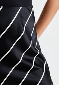 Musta kangashame, jossa valkoisia aaltoilevia raitoja, tyylikäs viimeistely ja sileä pinta. Oikealla näkyvissä oleva sivutasku.