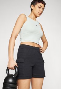 Lys grønn ribbet crop-top med logo, kombinert med svarte bomull cargo-shorts med sidelommer. Modellen holder en kettlebell.