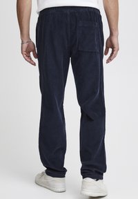 Navy corduroy pants with a relaxed fit, featuring an elastic waistband, rear pocket, and narrow legs, paired with light-colored sneakers.