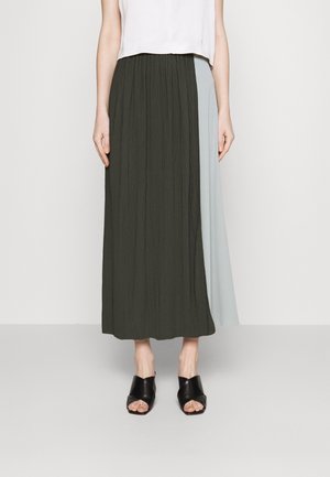 Jupe maxi, texture froncée, verte foncée d'un côté, bleu clair de l'autre, associée à des sandales noires à bout ouvert.