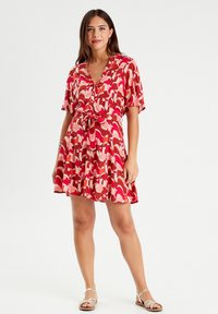 Red and pink patterned dress with short sleeves, a tie at the waist, and button details, made of lightweight fabric, features a flared skirt.