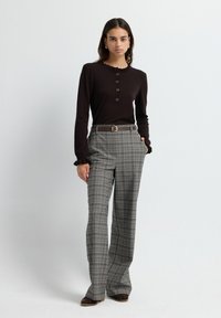 Langdellige bruine top met een ruches halslijn en een vijf-knopen knoopsluiting, gecombineerd met hoogstaande, geruite wijde broek in grijs.