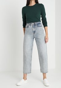 Grön stickad långärmad topp matchad med högmidjade, löst sittande, ljusblå denimjeans och vita slip-on skor.