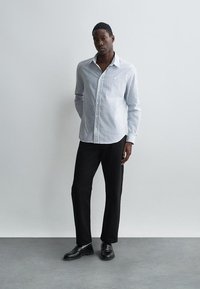 Svītrota krekla ar pogām zilā un baltā krāsā, kombinēta ar melnajām biksēm. Krekla piedurknes ir garas, un tam ir brīva piegriezuma forma, tam ir gluda tekstūra.