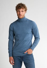Suéter de cuello alto azul hecho de una tela suave, diseño ajustado con puños y dobladillo acanalados, combinado con jeans azules. Aspecto simple y clásico.