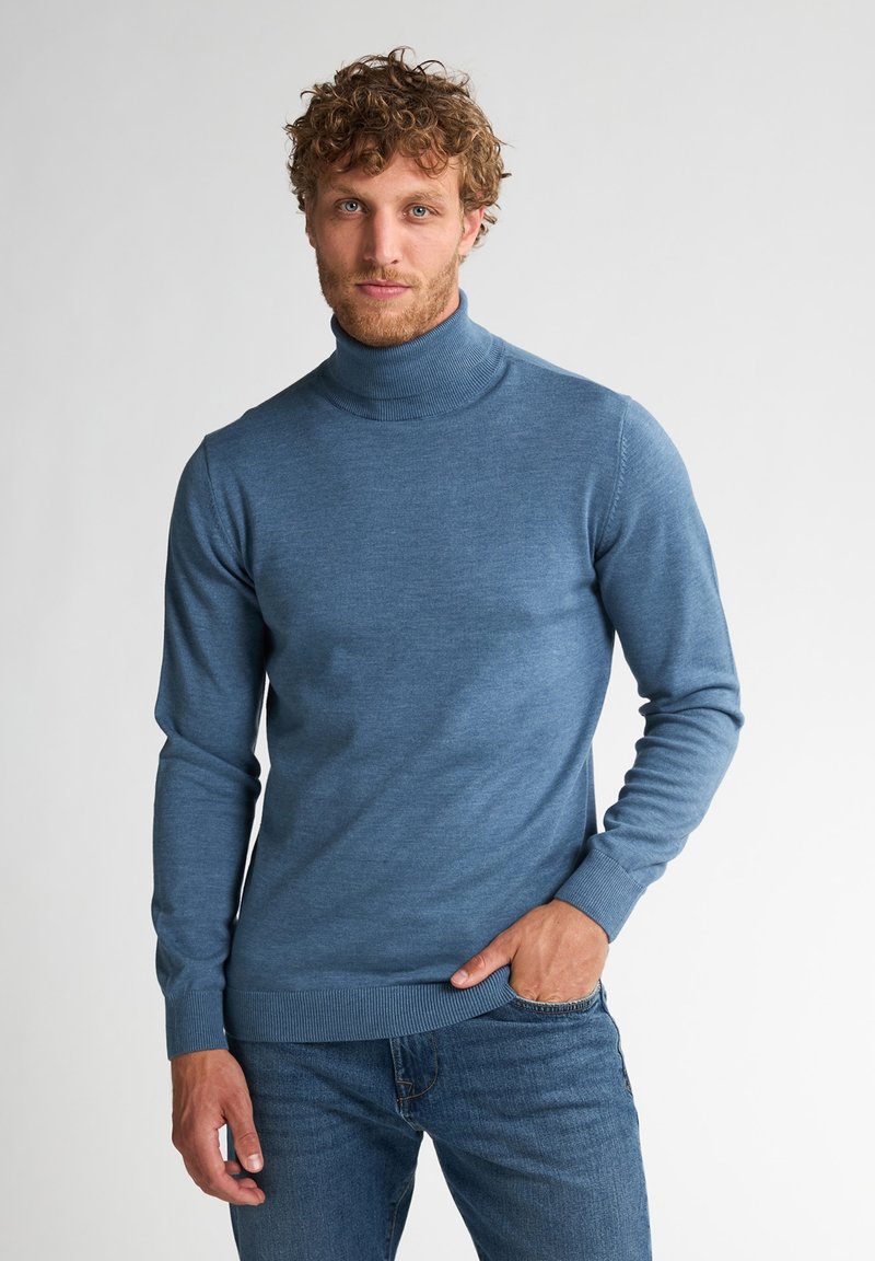Suéter de cuello alto azul hecho de una tela suave, diseño ajustado con puños y dobladillo acanalados, combinado con jeans azules. Aspecto simple y clásico.