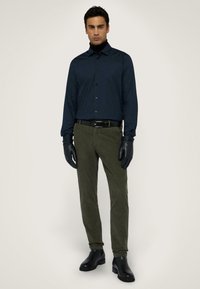 Camicia navy con bottoni, pantaloni verde oliva, guanti in pelle nera e stivali alla caviglia. Design slim fit con una texture liscia e dettagli classici.