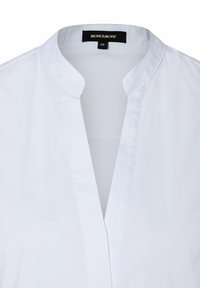 Weiße Bluse mit Kragen, glatter Textur und dezenten Nähten. Das Etikett trägt die Aufschrift "MORE & MORE", Größe 36.