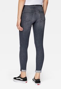 Tunna mörk denimjeans med medelhög midja, uppvikta nederkanter och två bakfickor, tillsammans med svartvita sneakers.