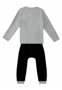 Graues Langarmoberteil mit Rundhalsausschnitt und eine schwarze Jogginghose mit grauen Bündchen an den Knöcheln. Glattes Material. Keine Muster.
