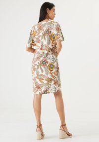Blumenkleid mit einem cremefarbenen Hintergrund, kurzen Ärmeln und bunten Mustern aus orangefarbenen, blauen und grünen Blumen. Tragen dazu hellbraune Wedgesandalen.