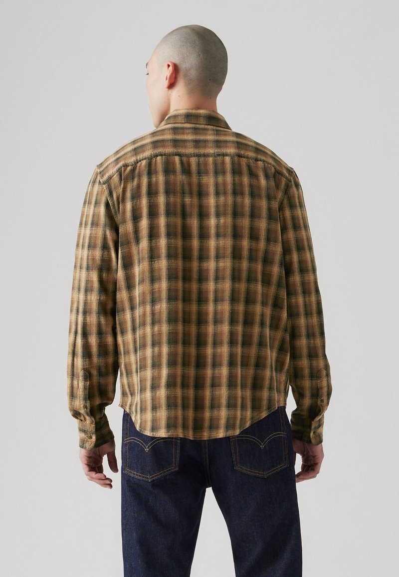 Camisa a cuadros marrón y verde con cuello, mangas largas y dobladillo curvado. La tela parece tener una textura con un acabado suave similar al de un paño de franela.