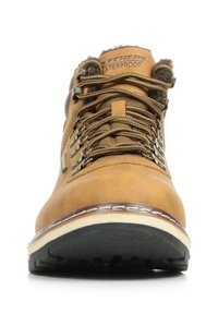 Stivale da trekking in pelle marrone con caratteristiche impermeabili, occhielli in metallo, lacci testurizzati, suola crema a contrasto e battistrada in gomma nera robusta.