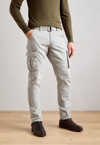 Light grey cargo pants with multiple side pockets, a belt, and tapered legs. Worn with dark brown ankle boots. Smooth fabric texture.