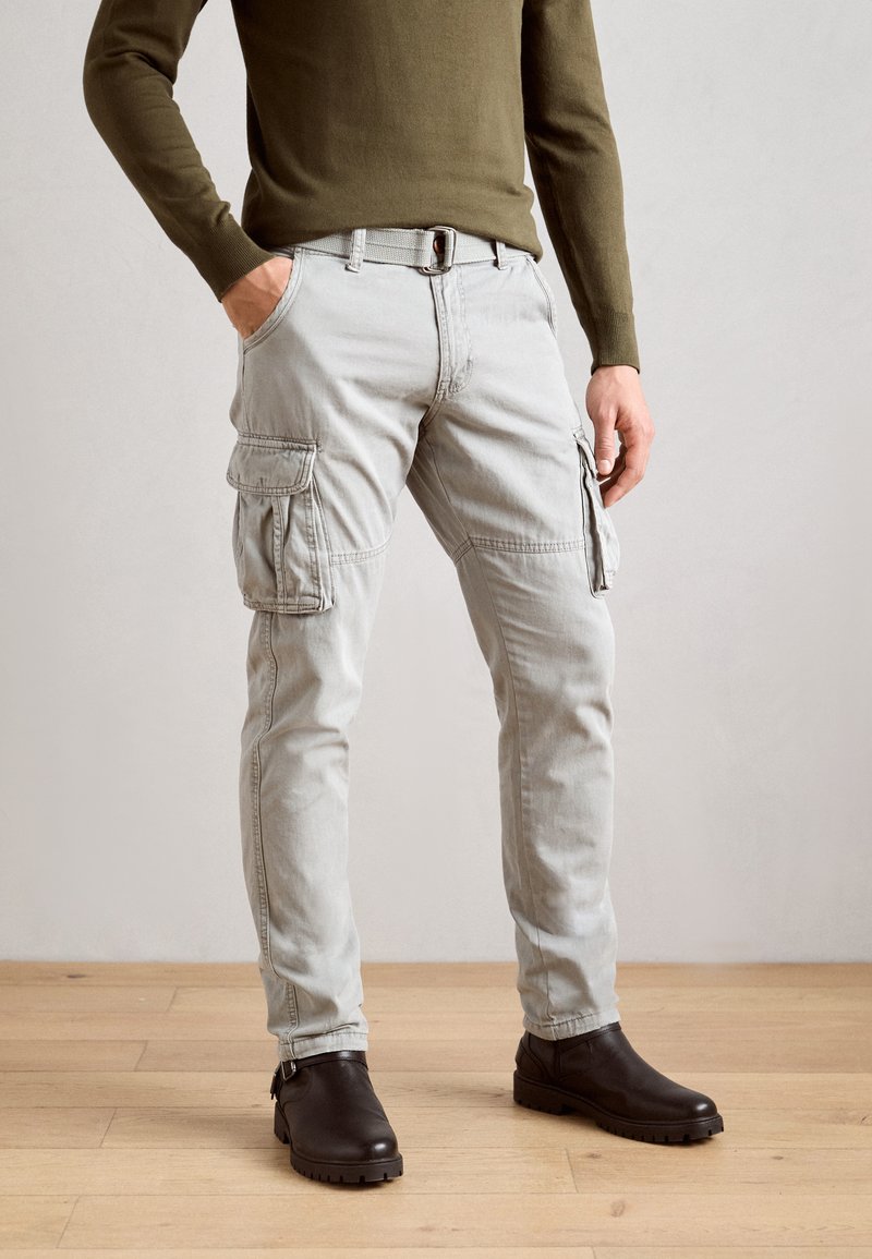 Light grey cargo pants with multiple side pockets, a belt, and tapered legs. Worn with dark brown ankle boots. Smooth fabric texture.
