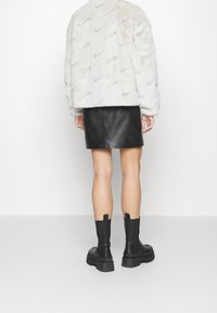 Faux fur, světle šedá bunda s vzorem loga Nike, kombinovaná s černou koženou minisukní a pevnými černými kotníkovými botami.