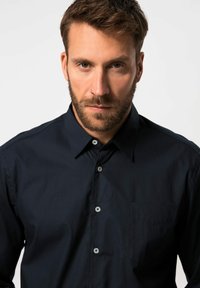 Tummansininen napitettava paita sileässä kankaassa, jossa on kaulus, etutasku ja vaaleat napit. Tekstuuri näyttää siistiltä ja kiiltävältä.