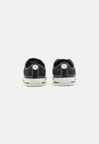 Czarne zamszowe sneakersy z kontrastującymi przeszyciami, białymi gumowymi podeszwami, dekoracyjnymi akcentami kwiatowymi oraz brandingiem "CONVERSE ALL STAR" na pięcie.