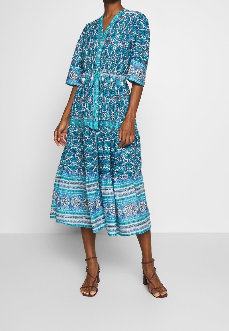 Abito midi stampato turchese con scollatura a V, maniche corte e vita con laccetti. Presenta disegni floreali e a righe, con orlo svasato.