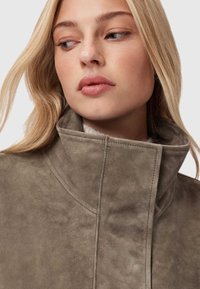 Olivově zelená semišová bunda s vysokým límcem a čistými švy. Hladká textura a minimalistický design zaměřený na funkčnost.