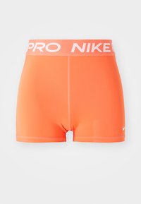 Oranžové sportovní šortky s širokým páskem, na kterém je bílý nápis „PRO NIKE“. Hladká textura, přiléhavý střih a malé bílé logo ve spodní části.