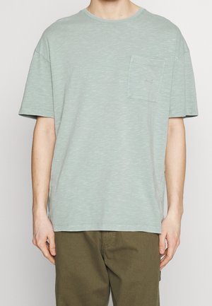 Hellgrünes kurzärmeliges T-Shirt aus strukturiertem Stoff, mit Brusttasche und rundem Ausschnitt. Dezentes meliertes Muster durchgehend.