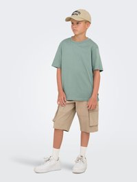 Mintgrøn kortærmet T-shirt, beige cargo-shorts, hvide sokker og hvide sneakers. Kasketten er beige med sort tekst.