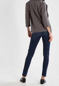 Ciemnoniebieskie wąskie dżinsy w połączeniu z szarym, teksturowanym topem o luźnym kroju i rękawach do połowy przedramienia. Całość dopełniają czarne buty.