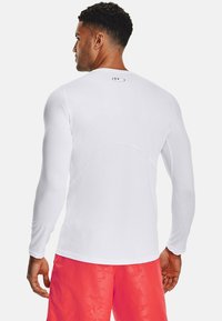 Langärmliges, tailliertes, weißes Sportshirt mit glatter Textur, das ein kleines Logo im oberen Rückenbereich sowie kontrastierende Nähte aufweist.