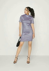 Vestido listrado com mangas curtas em azul, roxo e branco. Design justo, textura suave e decote alto. Usado com sandálias pretas.