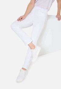 Weiße, figurbetonte Hosen aus einer Baumwollmischung mit glatter Textur. Kombiniert mit weißen Sneakers, die einen modernen, minimalistischen Stil präsentieren.