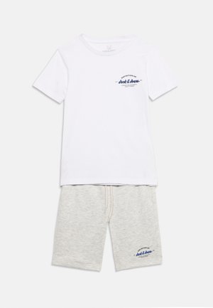 T-shirt bianca a maniche corte con testo blu navy sul petto abbinata a pantaloncini grigio chiaro con coulisse e testo blu navy coordinato sulla gamba sinistra.