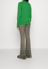 Maglione verde lavorato a maglia con collo a coste, abbinato a pantaloni a palazzo a fantasia nei colori blu, giallo e bianco. Tessuto liscio, vestibilità comoda.