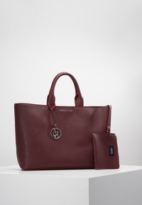 Burgundowa torba na ramię z ekologicznej skóry z czerwonymi akcentami, podwójnymi uchwytami, detalem z logo oraz odpinaną dopasowaną saszetką. Gładka tekstura, minimalistyczny design.