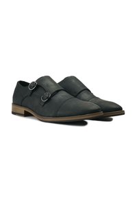 Black faux leather shoes with double buckle accents, pointed toe, low heel, and a textured finish. Features a contrasting brown sole.