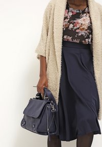 Borsa a tracolla in pelle blu navy con patta, dettagli con cerniera e hardware argentato. Abbinata a un cardigan strutturato beige chiaro e a una maglia floreale.