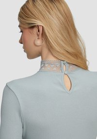 Lichtblauwe ribbeltop met kanten kraag en knoopsluiting op de rug, met een sleutelgat uitsnijding en een soepele textuur.
