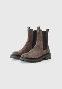 Bottes chelsea en suede marron avec des panneaux latéraux en élastique noir et des languettes de tirage, dotées d'une semelle en caoutchouc épaisse avec des nervures pour une meilleure traction.