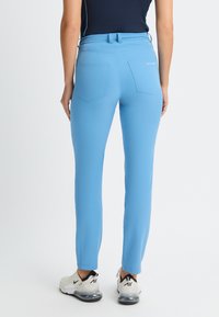 Ljusblå smala byxor med en mjuk textur, två bakfickor och en medelhög midja, i kombination med vita och svarta sportskor.