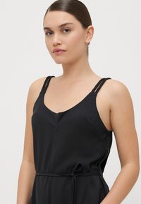 Vestido negro sin mangas con escote en V, tirantes trenzados y un detalle de cintura atada; confeccionado en una tela suave y ligera.